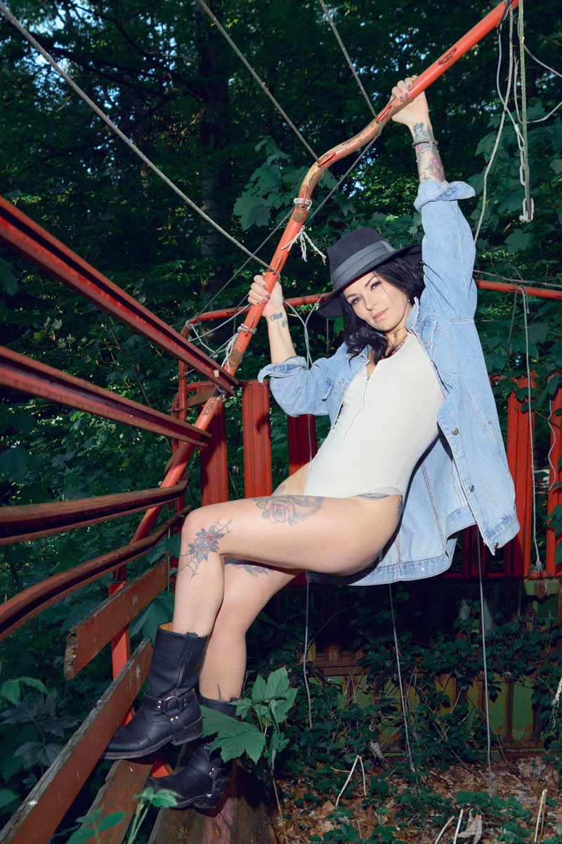 Dynamisches Outdoor-Portrait einer Frau in Jeansjacke auf roter Metallkonstruktion, kreative Portraitfotografie Traunstein