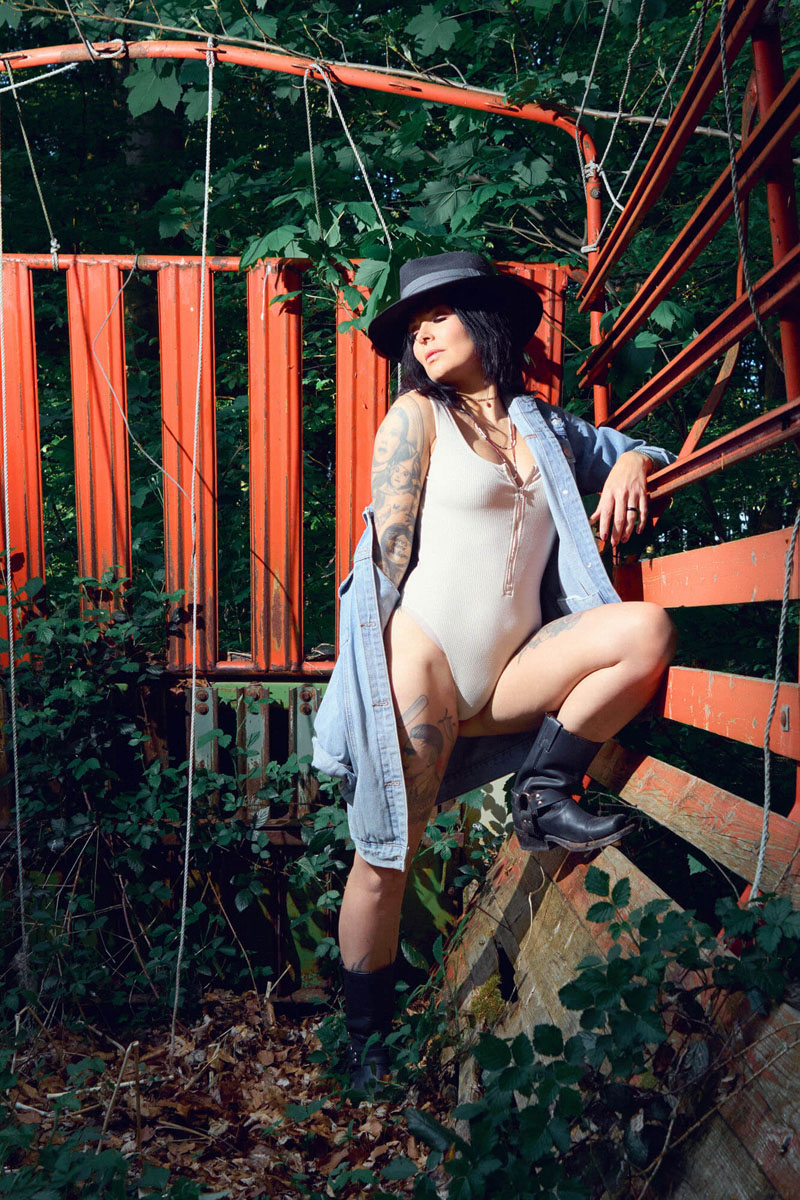 Kontemplatives Portrait einer Frau mit Hut auf roter Metallbrücke, stimmungsvolle Outdoor-Portraitfotografie Traunstein