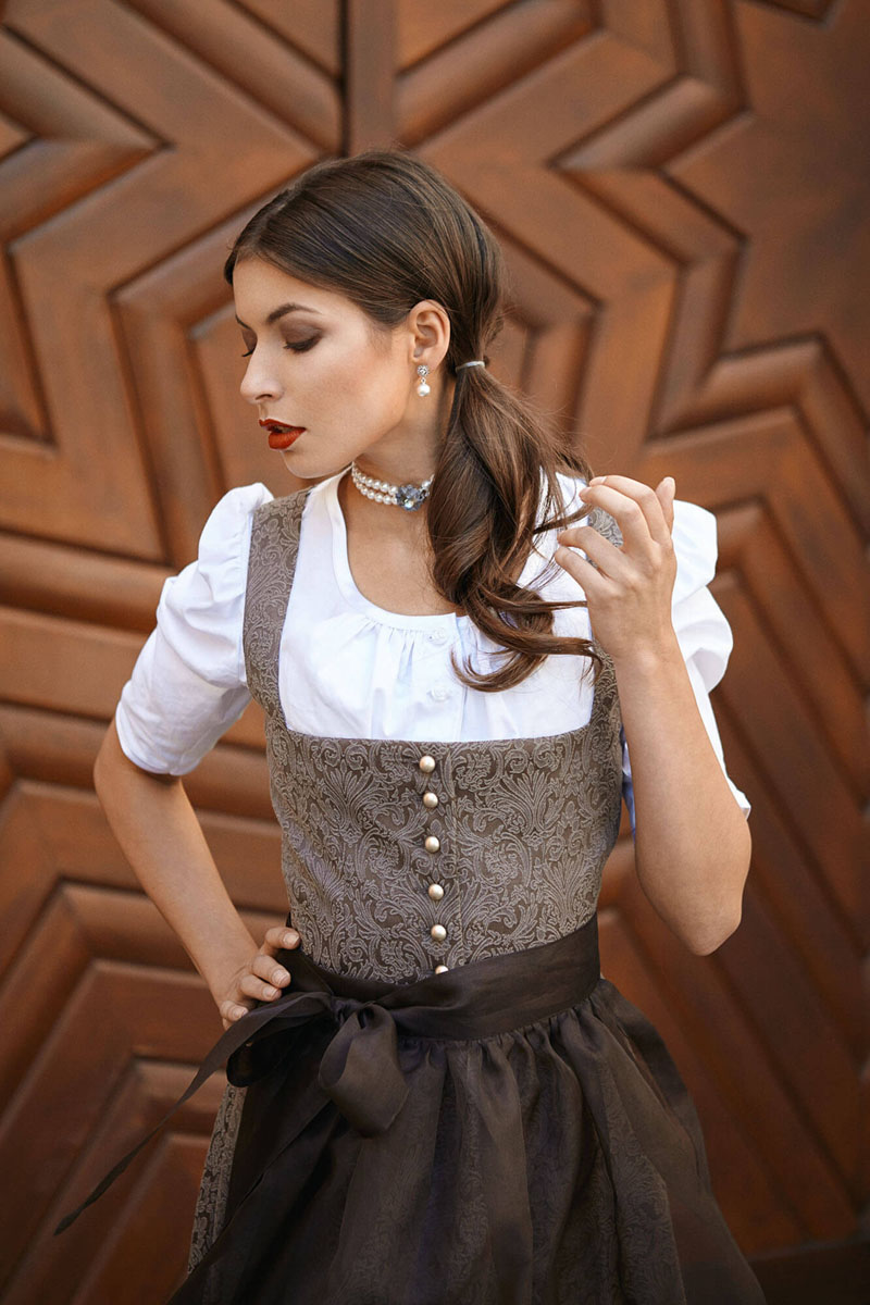 Trachten Portrait einer Frau im grauen Dirndl vor traditioneller Holzarchitektur, elegante Pose mit Perlenschmuck, Chiemgau Fotograf