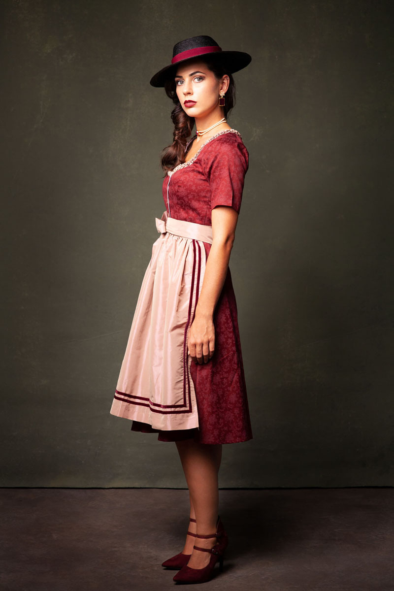 Seitliches Portrait Frau in rotem Dirndl mit rosa Schürze und schwarzem Hut - Alpenfotografie